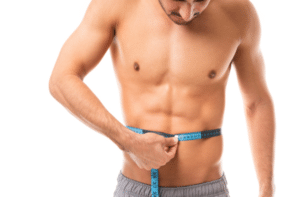 Muscular man measuring his body with tape measure in studio