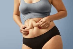 Woman holding loose stomach skin after weight loss, who may be a good candidate for body contouring surgery.
