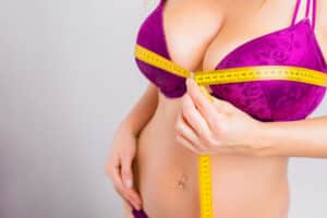 Woman in bra measuring large breasts and considering scarless breast reduction