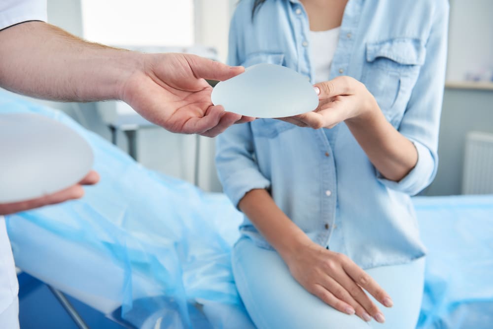 Plastic surgeon and female patient holding and examining a breast implant in a medical consultation room, discussing breast augmentation options.