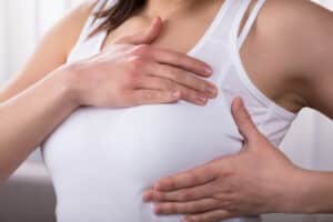 Woman holding her breast through a tank top, dealing with firmness and discomfort from capsular contracture.