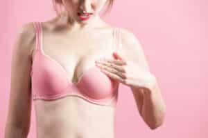 Woman in pink bra looking frustrated at uneven breasts